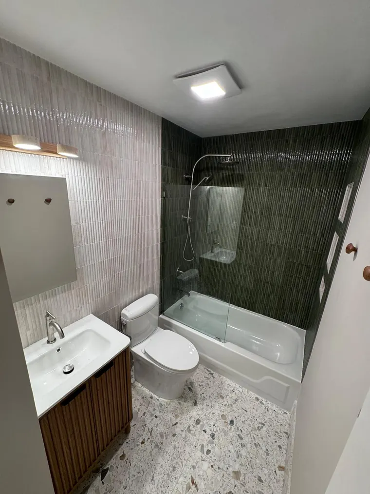 Alcove tub with vertical green tile surround and a wood vanity