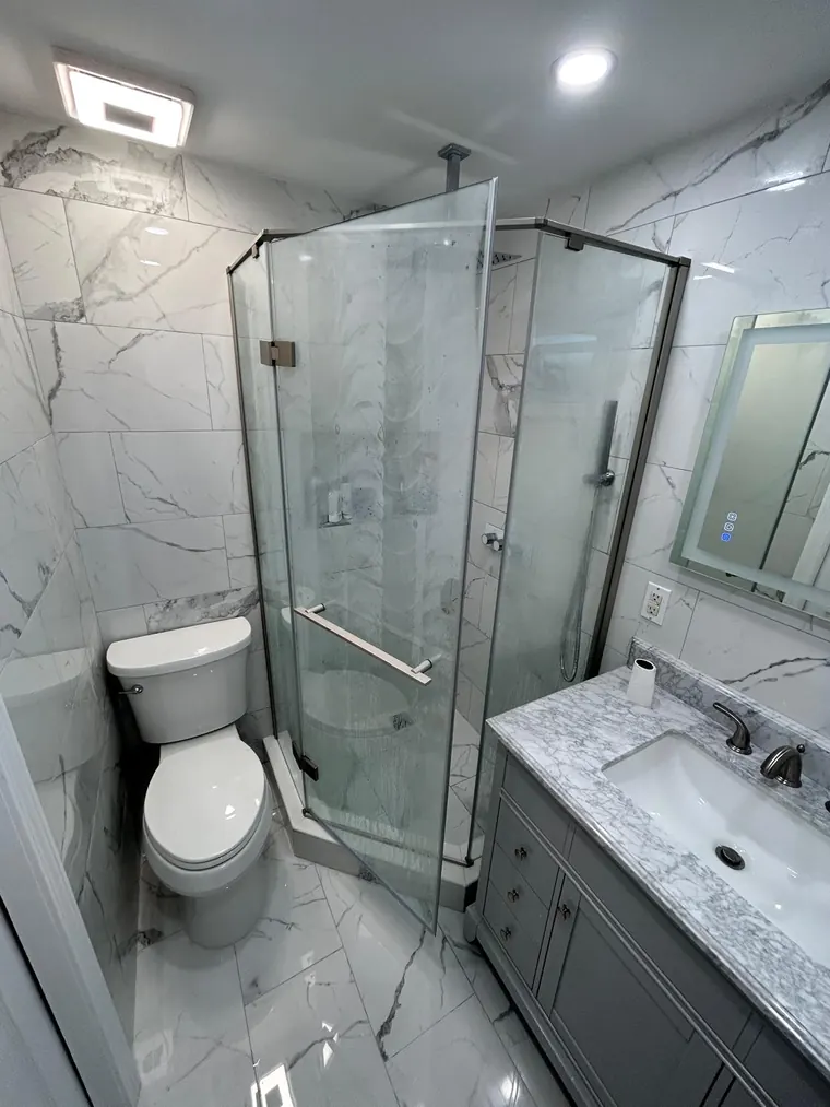 Corner glass shower with marble look wall tile and a vanity